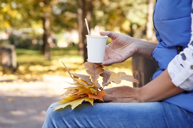 Mujer joven con una taza de café y hojas de arce otoñales en el parque de la ciudad