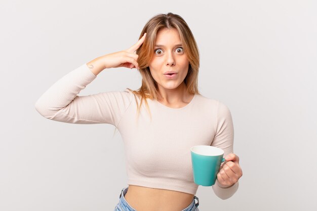 Mujer joven con una taza de café mirando sorprendido, dándose cuenta de un nuevo pensamiento, idea o concepto