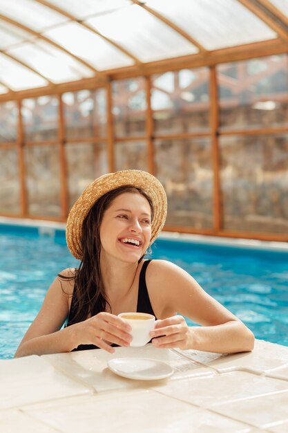 Mujer joven con taza de café en la piscina