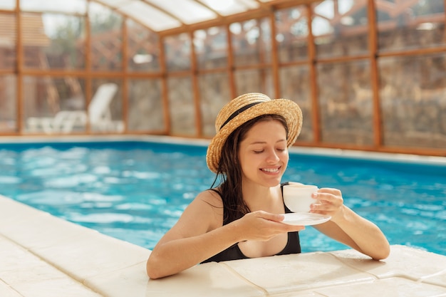 Mujer joven con taza de café en la piscina
