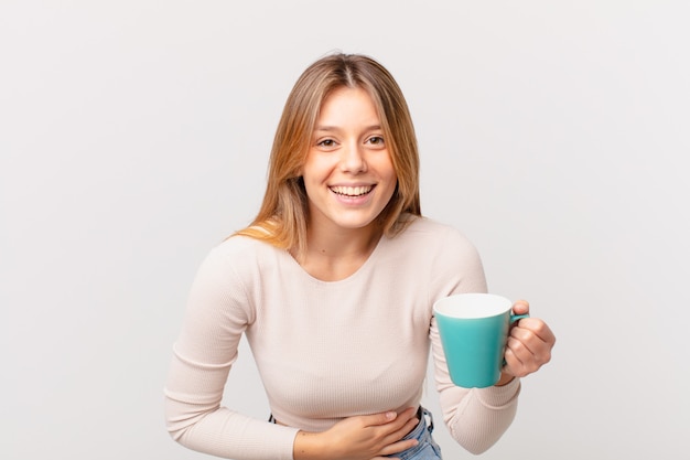 Mujer joven con una taza de café riéndose a carcajadas de una broma hilarante