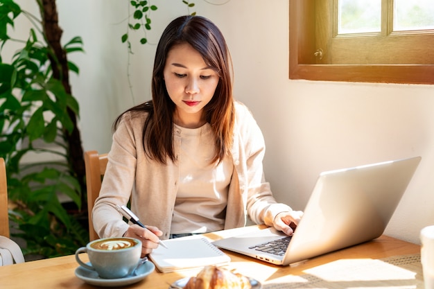 Mujer joven con taza de café sentado y trabajando en la computadora portátil en la cafetería.