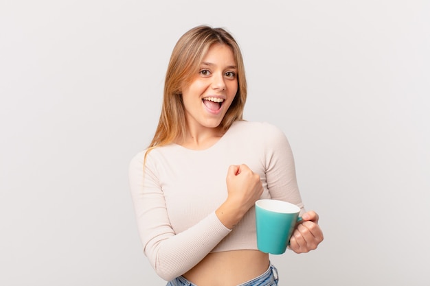 Mujer joven con una taza de café sintiéndose feliz y enfrentando un desafío o celebrando