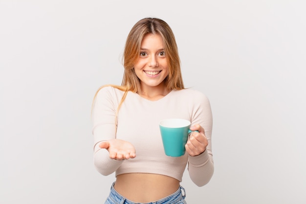Mujer joven con una taza de café sonriendo felizmente con amigable y ofreciendo y mostrando algo
