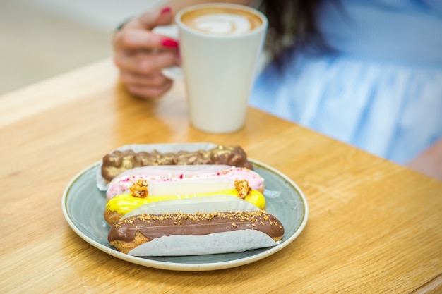 Mujer joven con una taza de café y un trozo de tarta sentado a la mesa en un café al aire libre