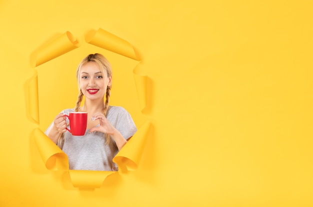 Mujer joven con una taza de té en el escritorio de papel amarillo rasgado comercial publicidad facial