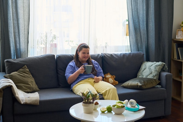 Mujer joven con una taza de té o café relajándose en un sofá cómodo y suave