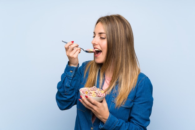 Mujer joven con tazón de cereales sobre pared azul aislado
