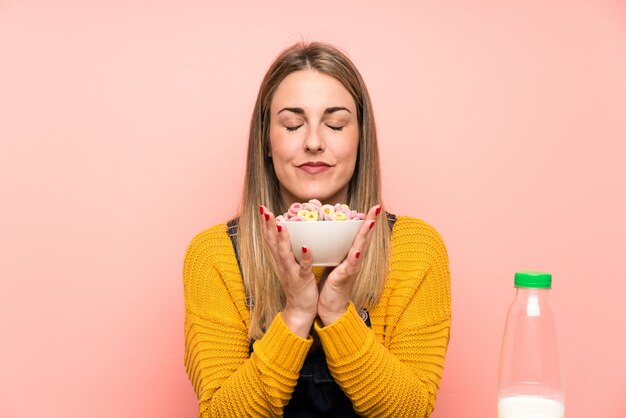 Mujer joven con tazón de cereales sobre pared rosa