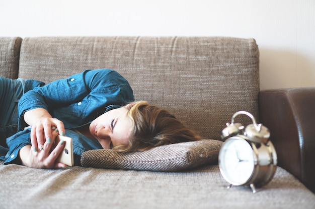 Mujer joven con teléfono en la cama, mirando la pantalla, insomnio, comprobar la hora, despertarse con el teléfono inteligente, adicción al teléfono móvil - despertador cerca