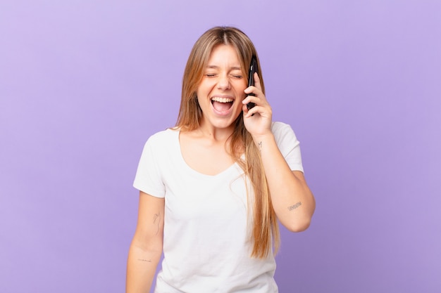 Mujer joven con un teléfono celular gritando agresivamente, mirando muy enojado