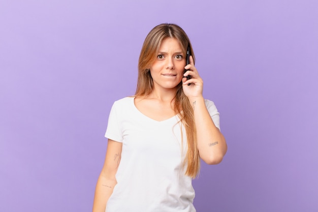 Mujer joven con un teléfono celular mirando perplejo y confundido