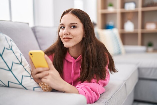 Mujer joven con teléfono inteligente acostado en el sofá en casa