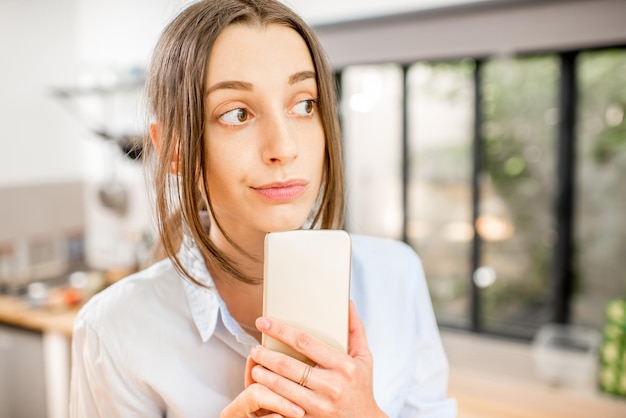 Mujer joven con un teléfono inteligente en la cocina