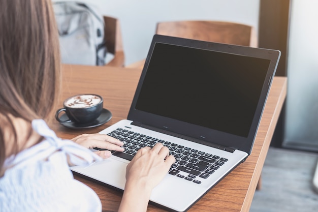 Mujer joven con teléfono inteligente y computadora portátil con una taza de café en la cafetería