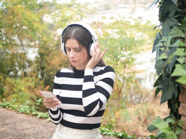 Mujer joven con teléfono inteligente escuchando música en auriculares