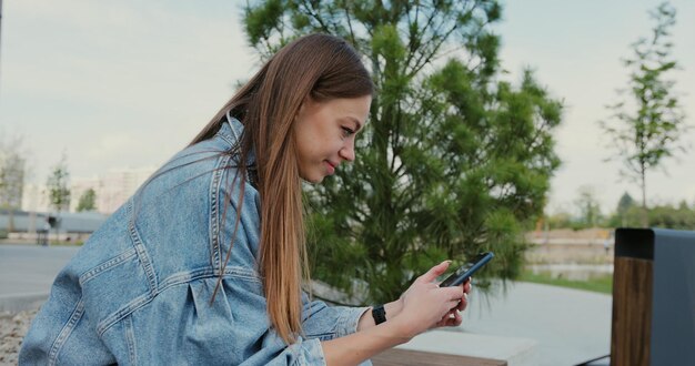 Mujer joven con teléfono inteligente navegando usando aplicaciones móviles para compras en línea redes sociales sentado en un banco en la ciudad moderna Comunicación compras en línea chat concepto de redes sociales