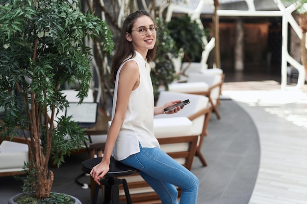 Mujer joven con un teléfono inteligente de pie en el salón del restaurante