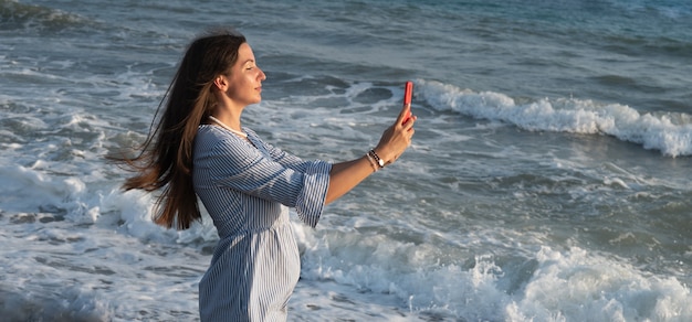 Mujer joven con teléfono junto al mar.