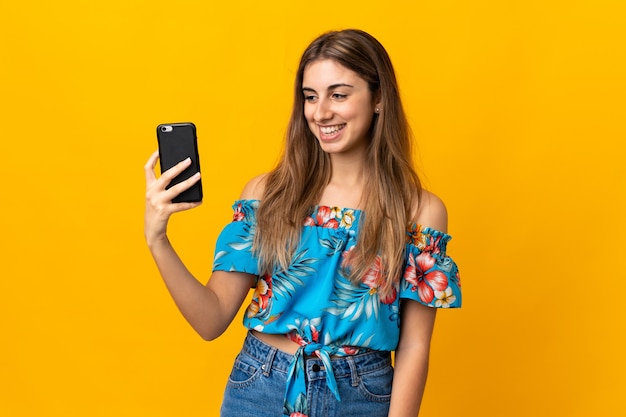 Mujer joven con teléfono móvil aislado en la pared amarilla con expresión feliz