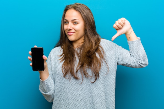 Mujer joven con un teléfono móvil contra el fondo azul.