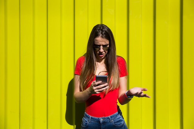 Mujer joven con teléfono móvil junto a la pared amarilla