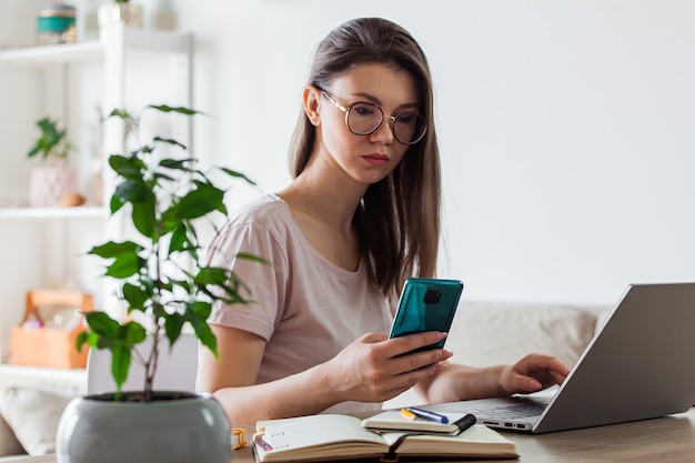 Mujer joven con teléfono móvil y portátil para trabajar en casa, varios dispositivos