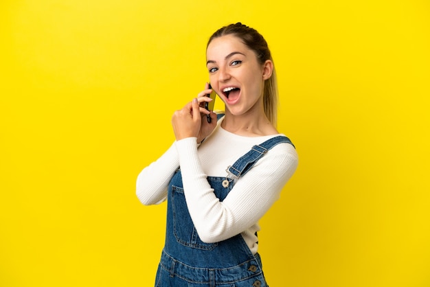Mujer joven con teléfono móvil sobre fondo amarillo aislado celebrando una victoria