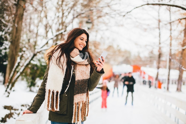 Mujer joven con un teléfono en el parque de invierno