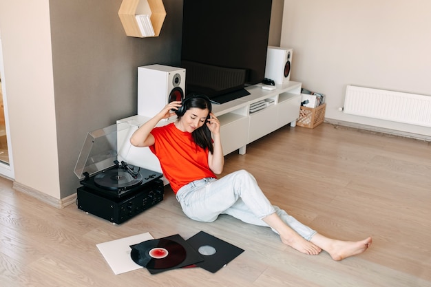 Mujer joven tendida en el suelo, escuchando música en un reproductor de vinilo