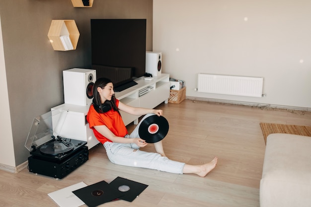 Foto mujer joven tendida en el suelo, escuchando música en un reproductor de vinilo