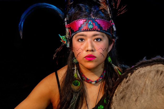 Foto mujer joven teotihuacana, xicalanca - tolteca en fondo negro, con vestimenta tradicional danza con adornos con plumas y tambor