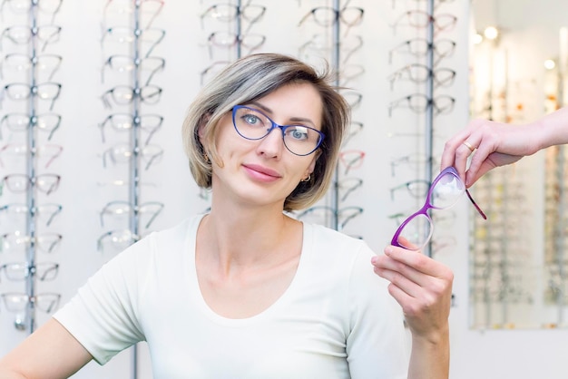 Mujer joven en tienda de óptica eligiendo nuevas gafas con gafas ópticas en la tienda de óptica Una mujer elige gafas Emociones Oftalmología