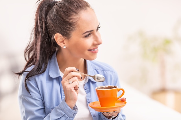 Foto mujer joven tiene café de la mañana en una taza de naranja y una cuchara en la mano.