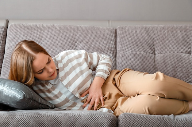 Foto mujer joven tiene dolor abdominal acostado en el sofá en la jornada laboral en la oficina. dolor agudo en pms hinchazón. adolescente con problemas de dolor intestinal.