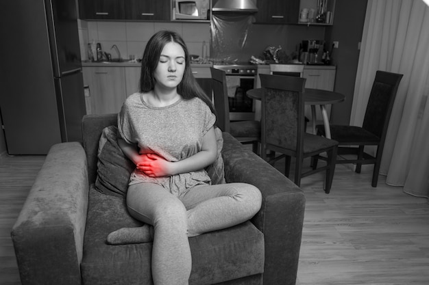 La mujer joven tiene dolor en el hipocondrio derecho, la mujer joven tiene dolor de estómago, fotografía en blanco y negro, acento rojo, enfermedad de la vesícula biliar