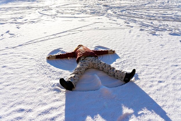 Foto mujer joven tirada en la nieve y haciendo un ángel de nieve paseos invernales y diversión