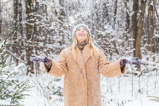 Mujer joven tirando nieve en el aire en un día soleado de invierno, ella es feliz y divertida.