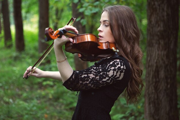 Una mujer joven toca una pieza romántica en un violín en un parque