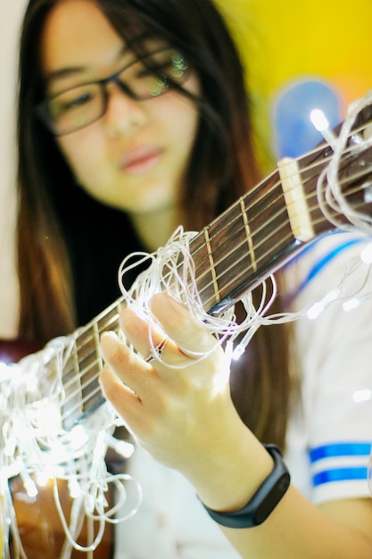 Mujer joven tocando la guitarra con luces de cuerda iluminadas en casa