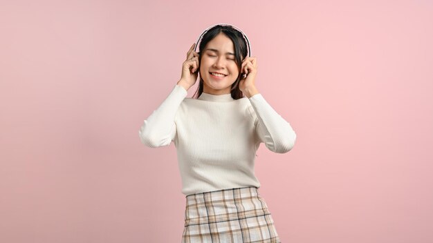 Mujer joven tocando su auricular sobre fondo rosa aislado