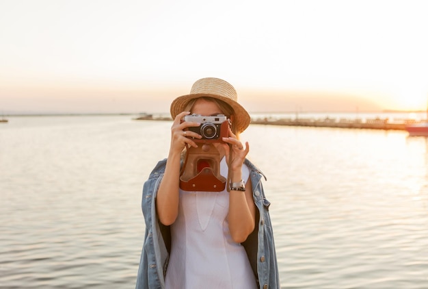 Mujer joven toma una foto en cámara al amanecer en el mar. concepto de viajes y turismo