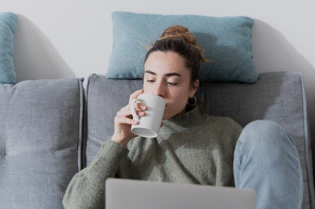 Mujer joven tomando un café mientras trabaja en la computadora portátil