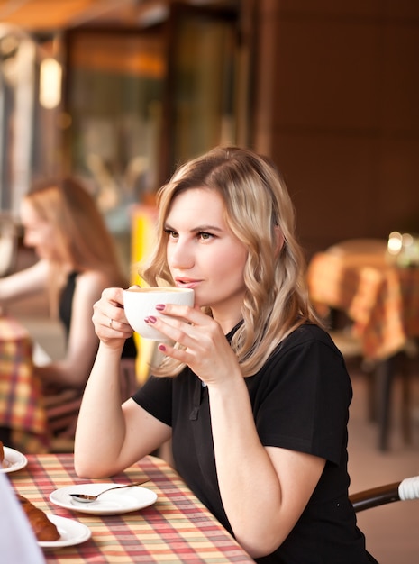 Mujer joven tomando un café en la terraza de un café con amigos