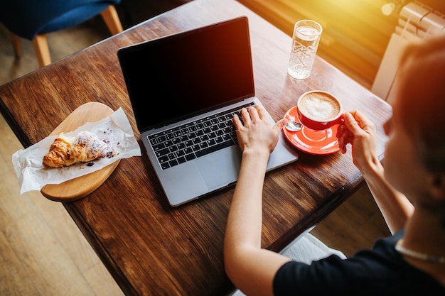 Mujer joven tomando café y trabajando en su computadora portátil en un café