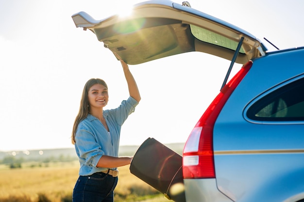 Mujer joven tomando colchoneta de yoga del maletero del auto para meditar sola en la naturaleza