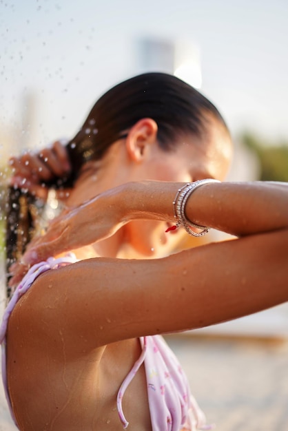 Mujer joven tomando una ducha al aire libre en la playa