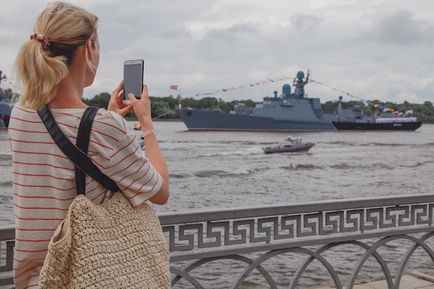 Mujer joven tomando una foto de buques de guerra en el río Volga en Rusia. Buques de guerra rusos en el río Volga en Astrakhan en verano en día nublado. Buques militares rusos.