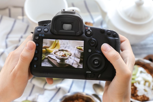 Mujer joven tomando una foto de un delicioso postre en un tazón con cámara profesional