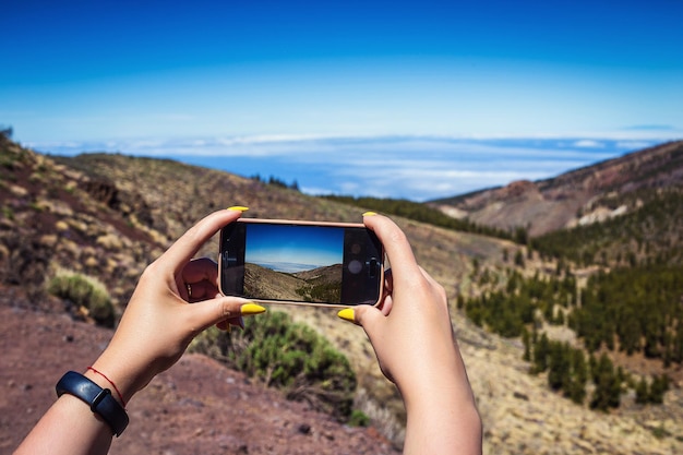 Mujer joven tomando una foto con su teléfono del increíble paisaje montañoso en Tenerife Islas Canarias España Concepto de viaje